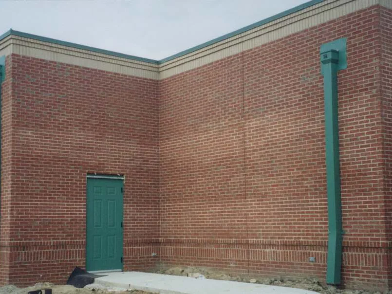 A green service door in a brick wall in 2001, the courses banded pale and dark above a buff base, with bare dirt where the landscaping will go