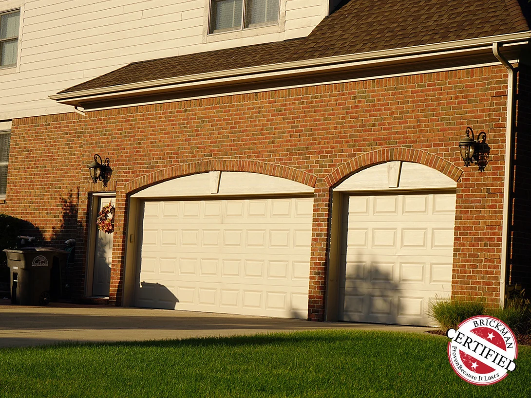 The same garage wall in 2019 with its doors fitted, the brick arches and the wall above them one even red range, the certification stamp at the corner