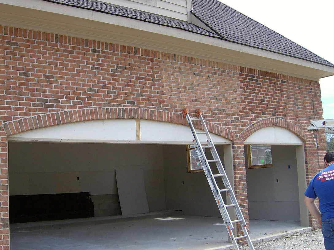 A ladder set against the same garage wall in 2007 while the work is under way, an applicator in a Masonry Cosmetics shirt at the right edge