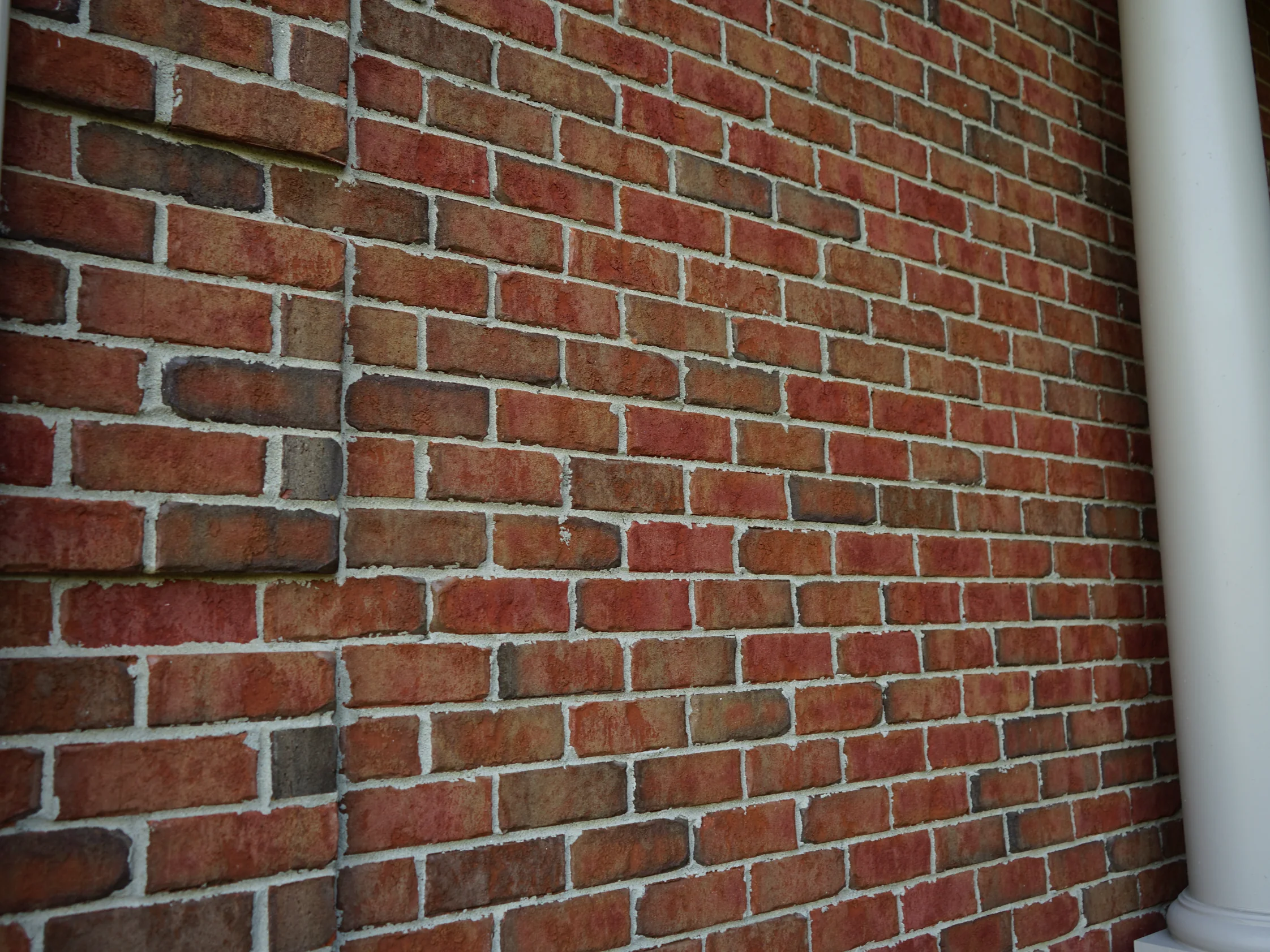 Close view along the brick beside a porch column in 2019, reds, browns and tans running through the courses with pale mortar joints