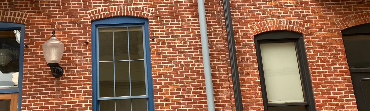 The red brick front of the downtown Michigan building in 2020, one range of brick running between blue framed windows and a downspout