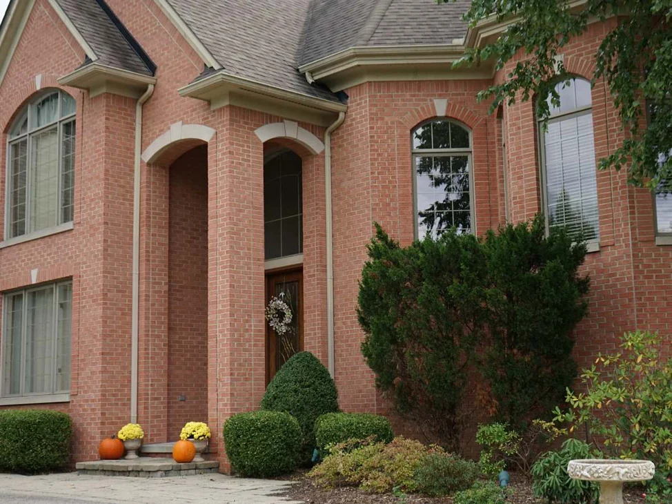 The front of the Michigan house in 2019, red brick through the gable and the arched entry with cast stone arches, clipped evergreens and a paver walk