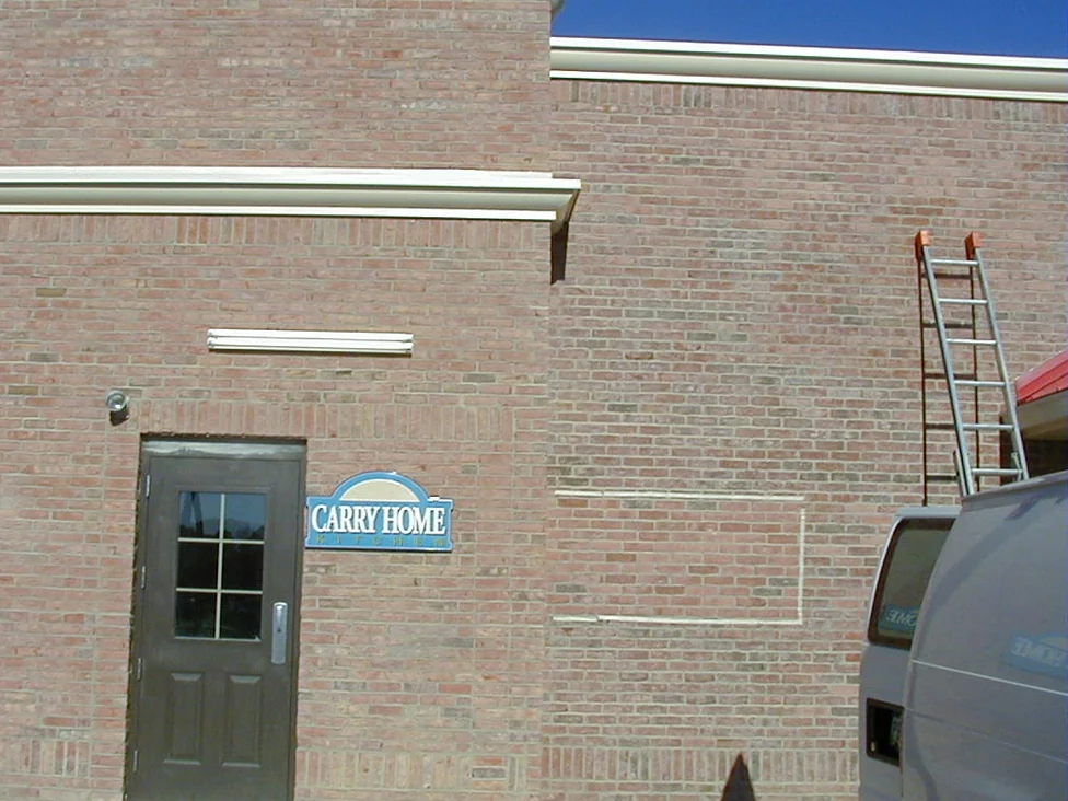 A service door in a pale pink and tan brick wall in 2002, the brick shifting in shade across the courses, with a stepped parapet, a small carry out sign and an aluminium ladder standing at the far end