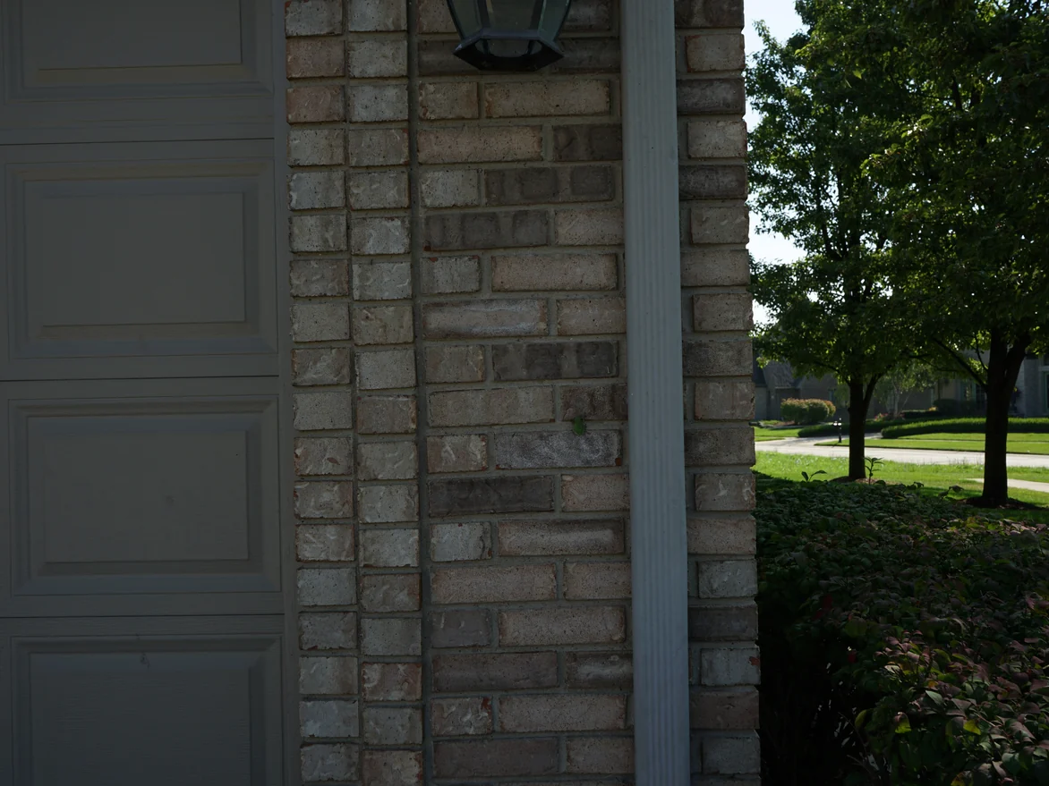 Close view of the brick pier beside a garage door in 2019, the individual units reading in salmon, cream and grey under a coach lamp