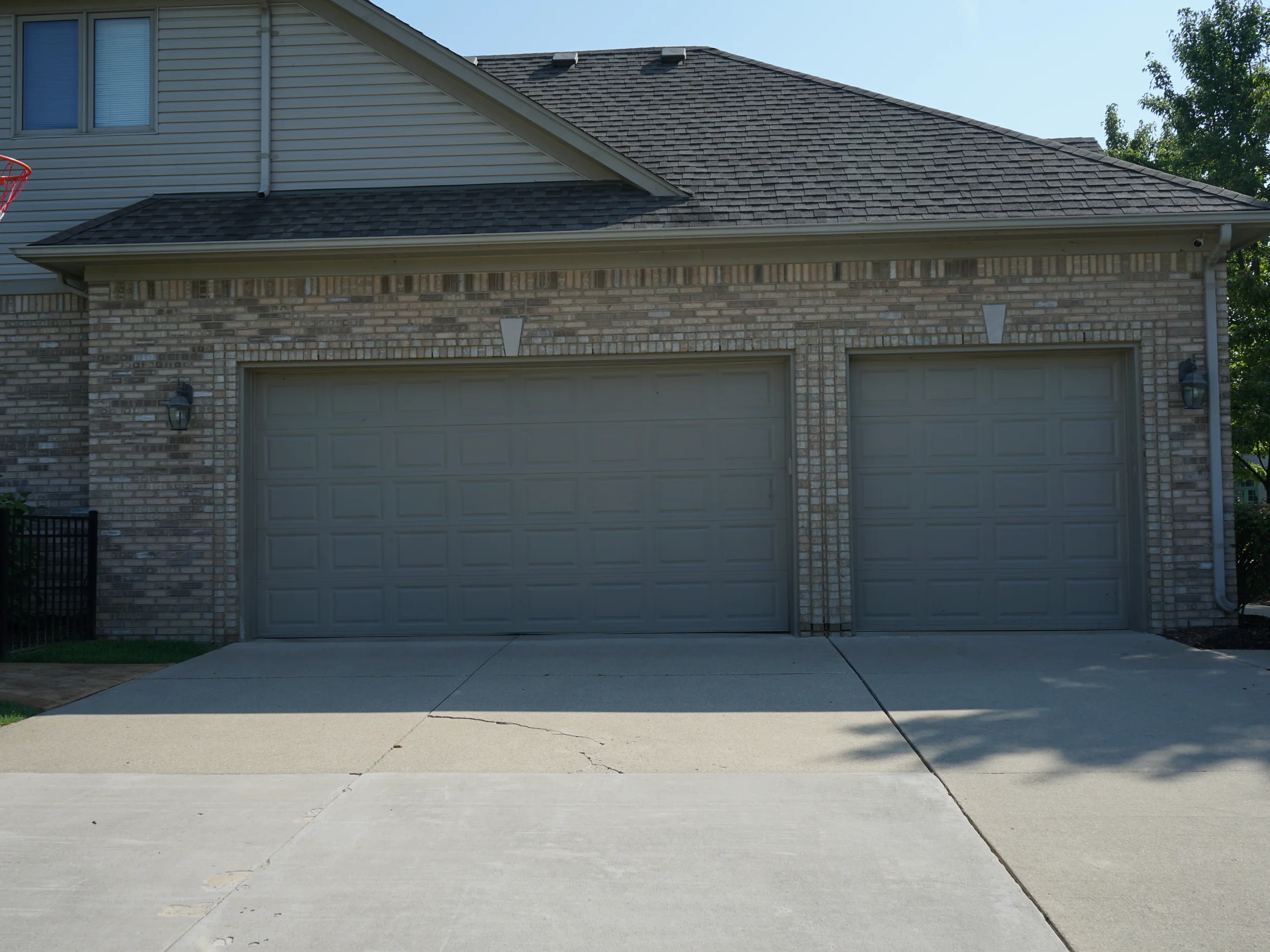The three-car garage elevation from the driveway in 2019, the brick an even salmon and tan range with lap siding on the storey above