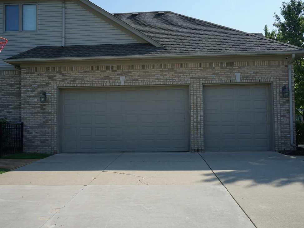 The three-car garage elevation of the Michigan house from the driveway in 2019, the brick an even salmon and tan range under a hipped roof.