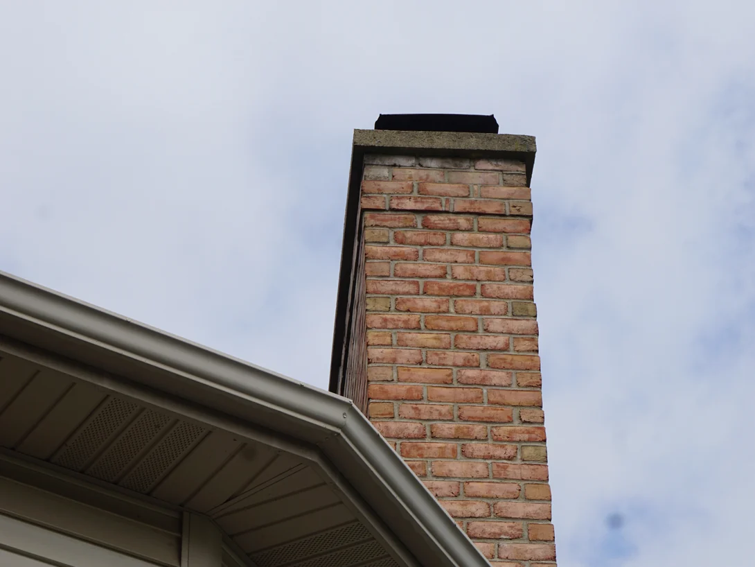 The top of the chimney against the sky in 2019, the brick above the eaves the same range as the brick beside them