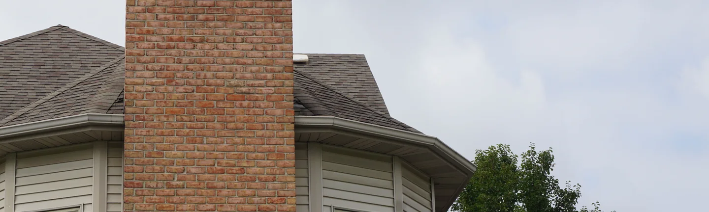 The chimney in 2019, its brick one warm red and tan range from the bay window below to the cap above the roof