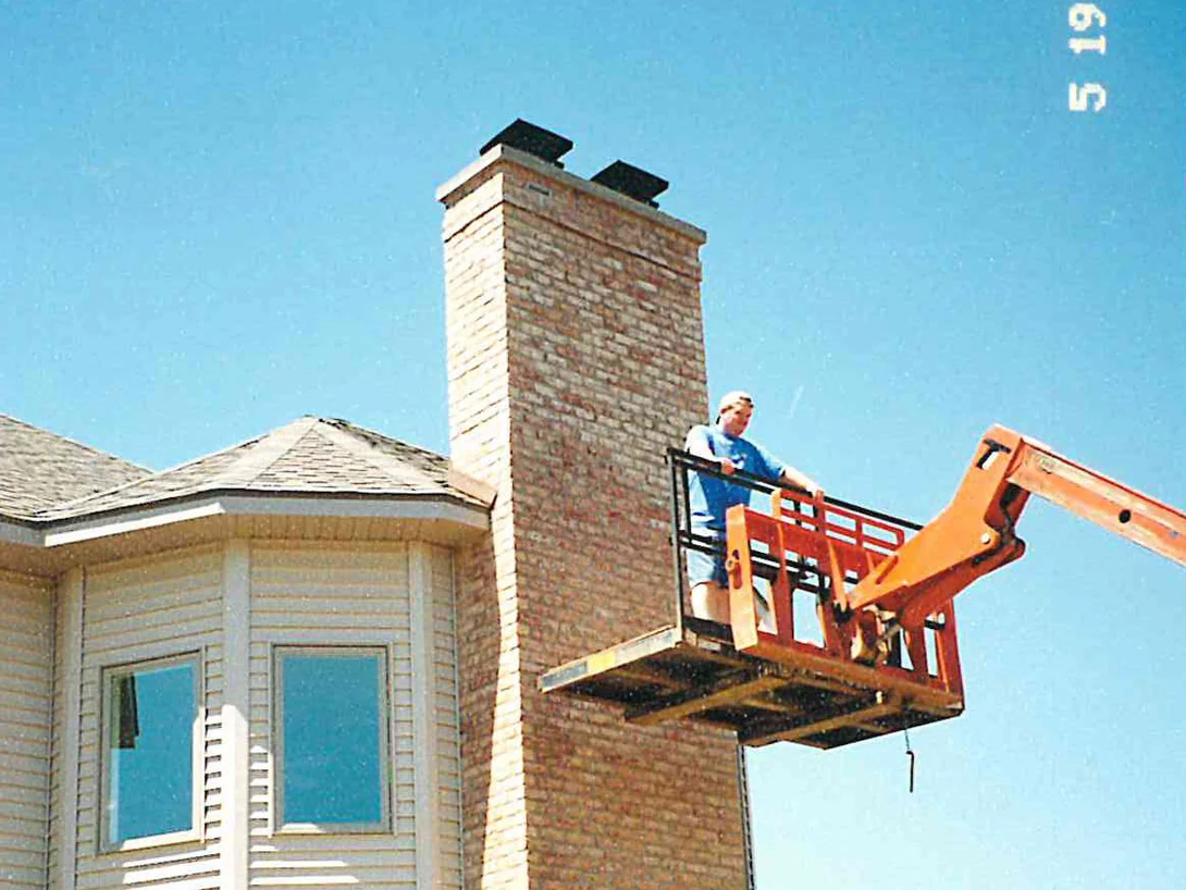 A worker on a boom lift platform beside the top of the chimney in 2001, the upper brick still pale against the warmer shaft below