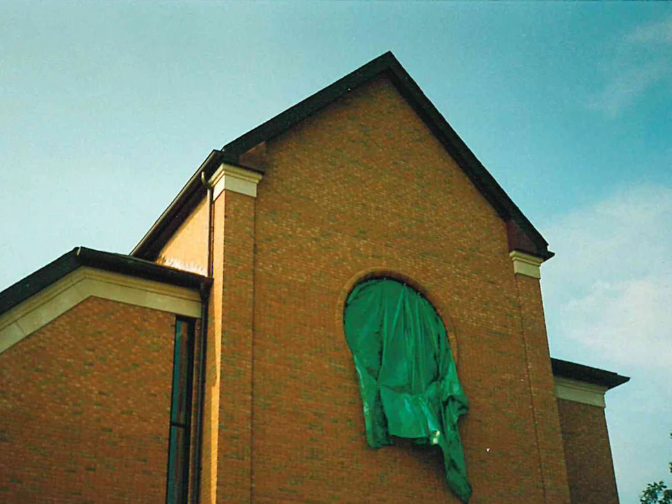 The gable end of the church in 1996, its brick reading noticeably light across the upper wall, with a green tarp hung over the round window opening