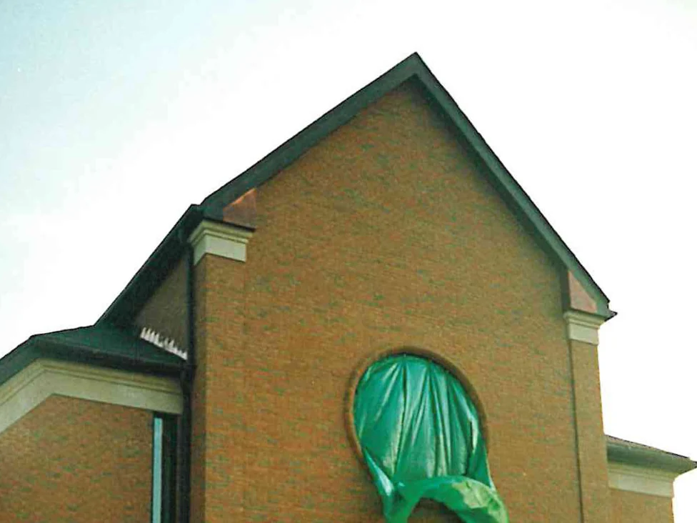 The same gable during the work, the round window opening still sheeted over in green plastic while the brick around it is worked