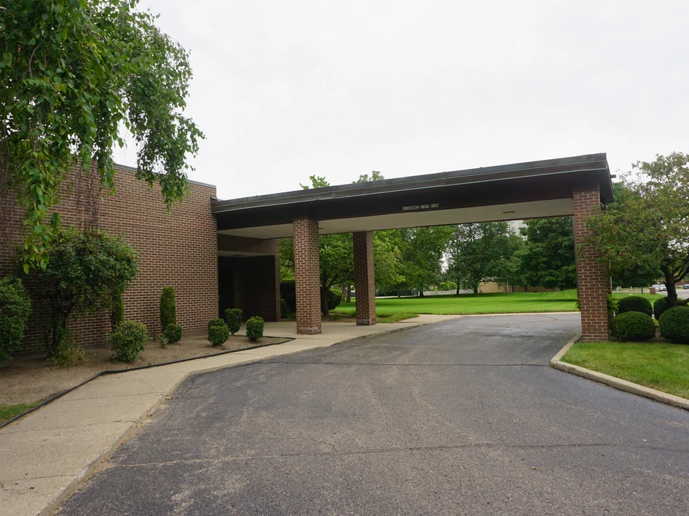 The drive-through entrance canopy from the driveway in 2019, its brick columns reading with the walls behind them as one blend