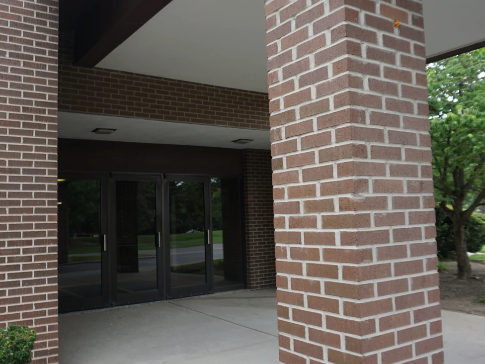 A canopy column at close range in 2019, its brick blended through red and brown on both faces, with the glass entrance doors beyond