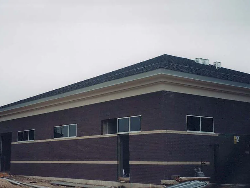 The outside corner of the building in 2000 after the work, dark brown brick with two cream accent bands under a cream cornice and dark hipped roof, construction materials still on the ground