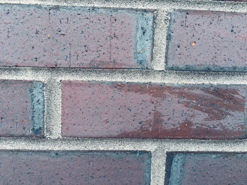 Three courses of the brick close up in 2019, plum brown units with blue grey flashing at the ends and grey sanded mortar joints between them