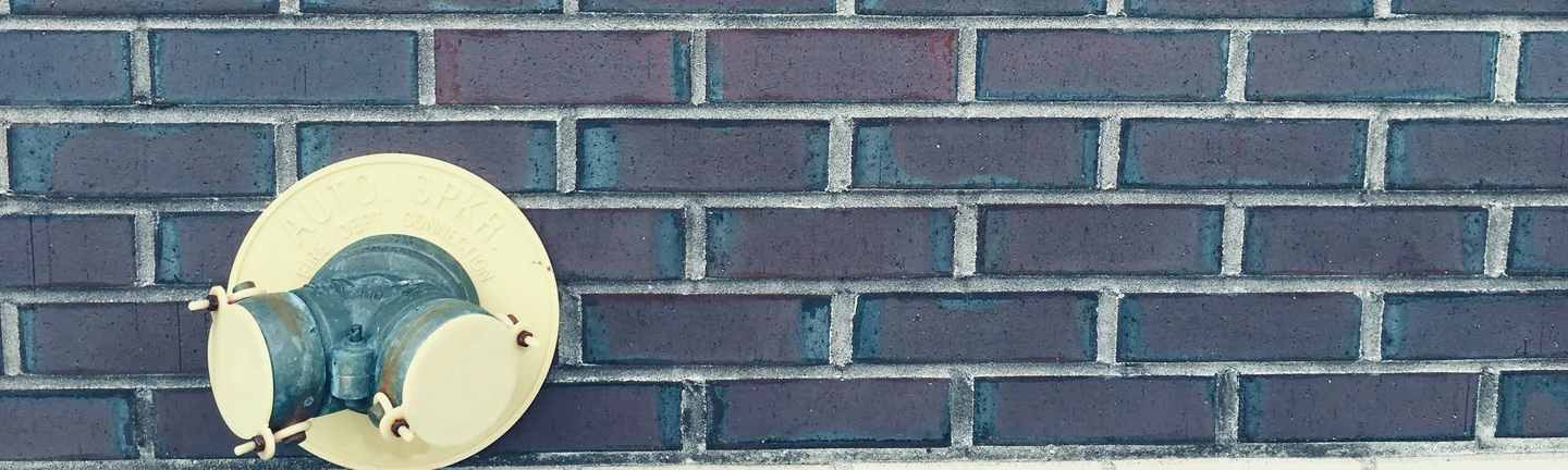 Dark brown brick with grey mortar joints in 2019, a cream sprinkler connection plate set into the wall