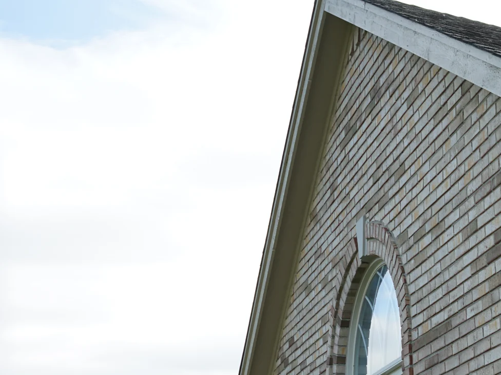 The outside corner of the gable end in 2019, buff and grey brown brick carrying evenly across both faces beside an arched window