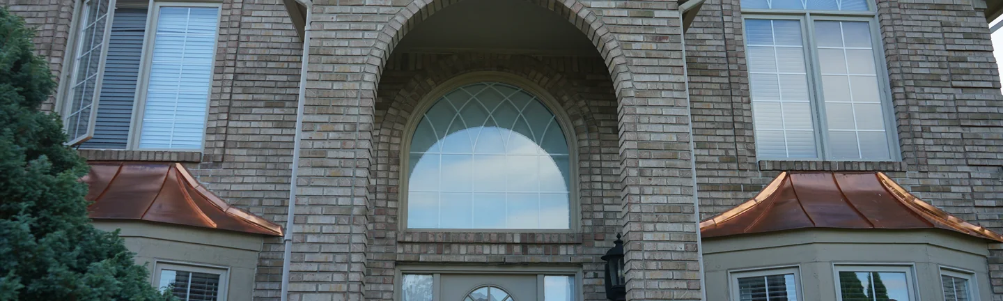 The front entry of the Michigan house in 2019, a tall arched brick recess between two gables with copper roofs over the bay windows