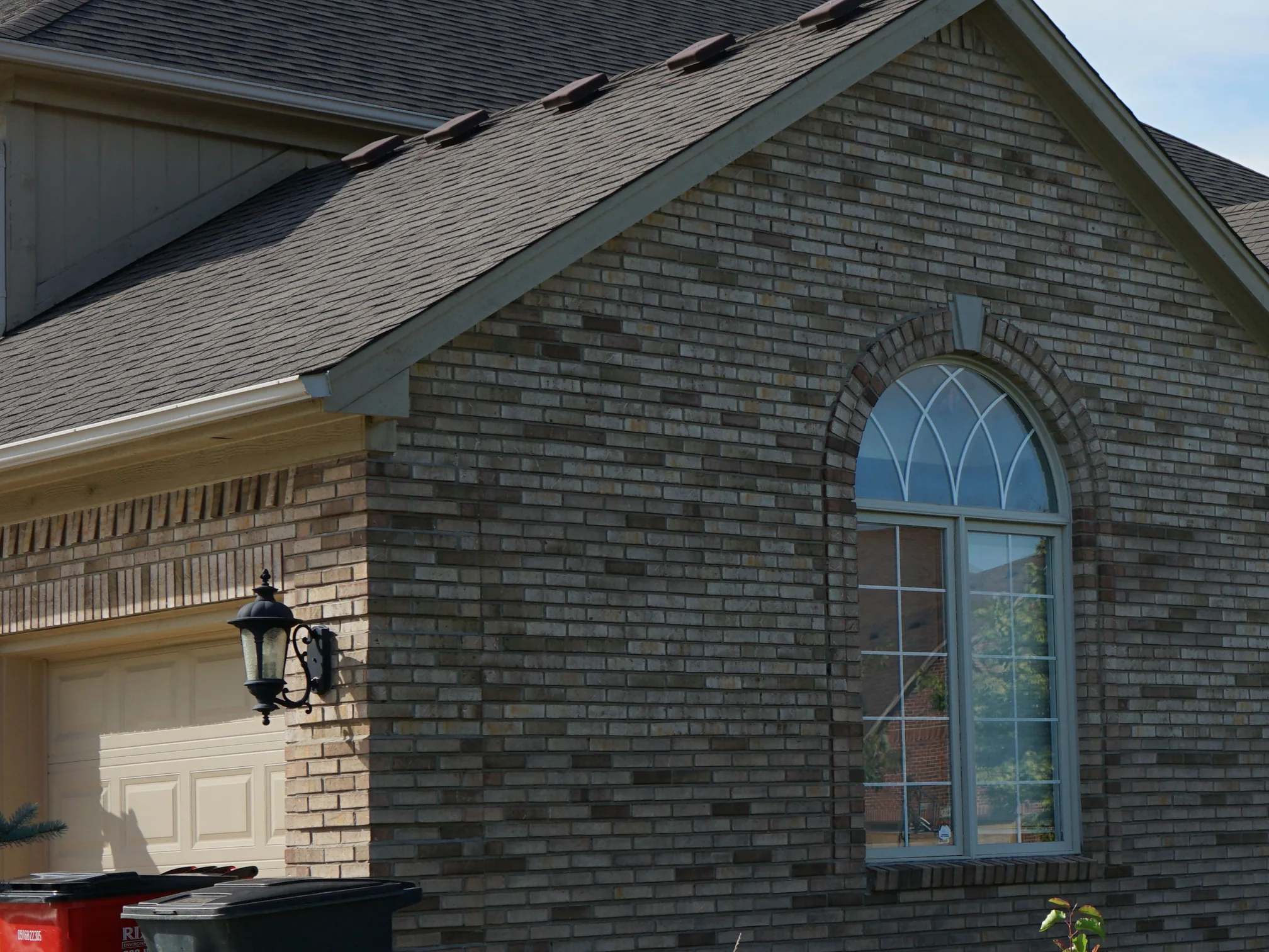 The gable end and attached garage in 2019, the buff brick reading as one range from the garage lintel up to the arched window in the gable