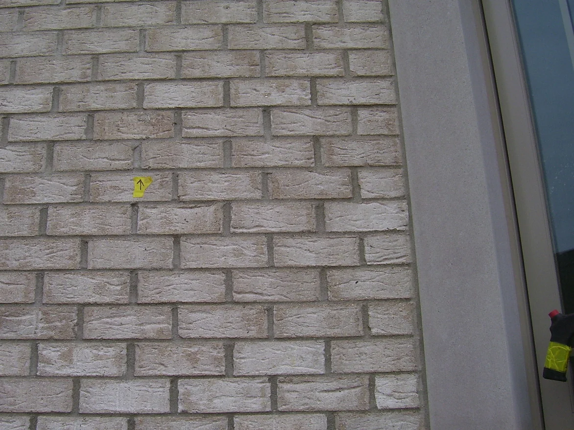 The same wall after the 2004 work, the marked brick carried into the surrounding color so the courses read as one range, with the yellow arrow marker still in place