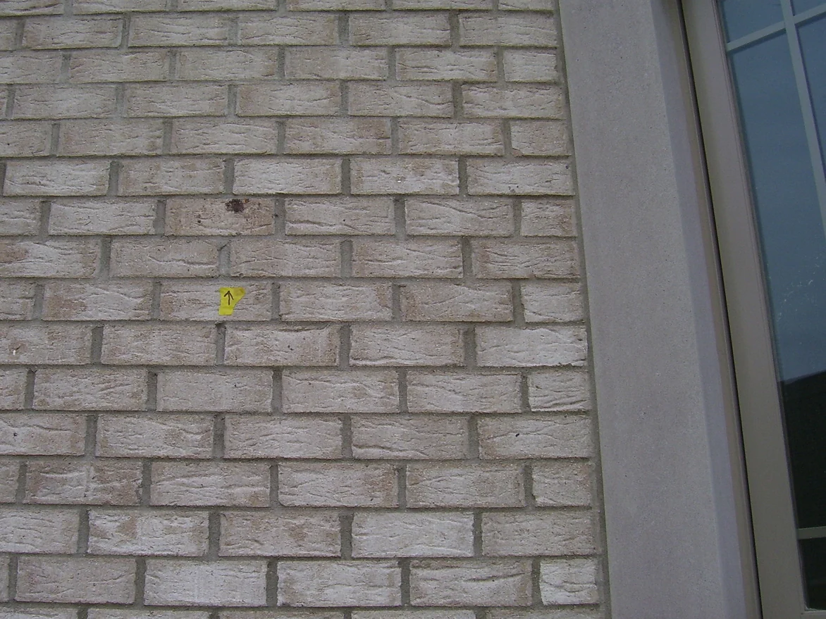 The wall beside a window in 2004, pale cream brick with a dark chipped brick and a smudge mark above a small yellow arrow marker