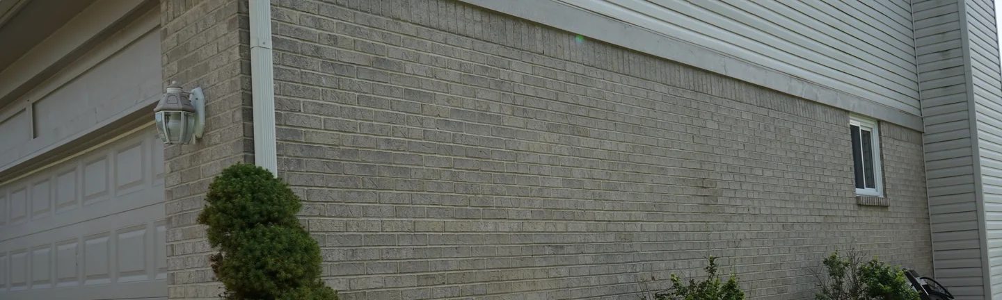 The grey brick side wall of the house in 2019, running unbroken from the garage corner to the far end