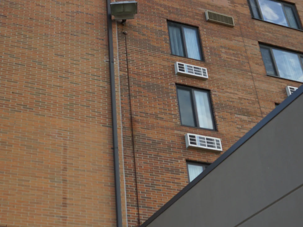 The stained elevator shaft in 2019 beside the tower wall, its face carrying the same mixed reds, tans and dark units as the wall next to it