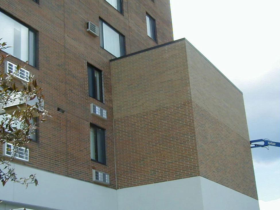 The new elevator shaft in 1998, a flat pale buff brick plane standing against the tower's mottled red brown wall, with a boom lift at the right