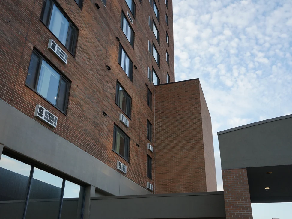 The high rise in 2019 with the elevator shaft standing clear against the sky, both walls in the same range of red and tan brick