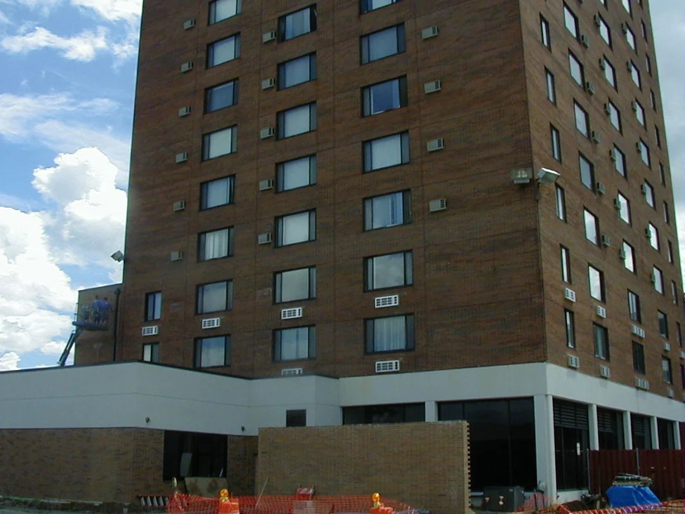 The tower from the car park in 1998, two workers on a lift platform high on the wall and construction fencing across the base