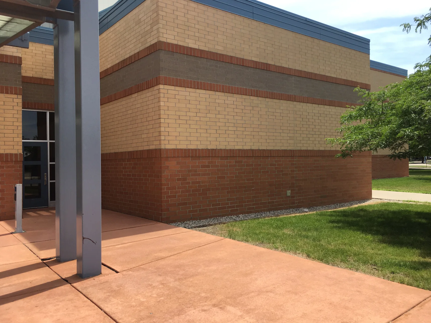 The corner in 2019 from under the entrance canopy, a steel column in the foreground and the banded brick wall beyond it