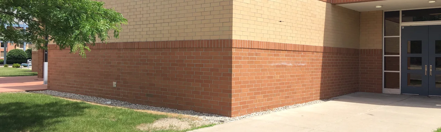 The outside corner of the high school in 2019, tan brick between a grey band and a red brown base, reading as one range on both faces