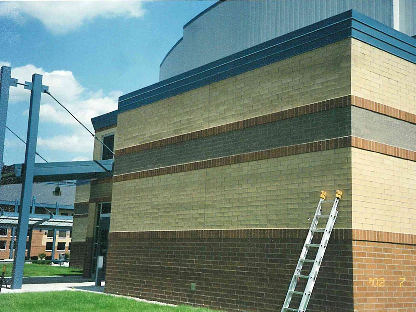 The corner of the high school in 2002, pale yellow green brick above a grey band and a dark brown base, an extension ladder against the wall and a camera date of 7/2/2002 in the corner