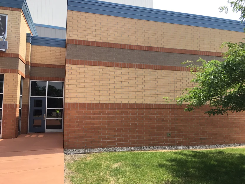 The banded wall in 2019 seen square on, tan brick, a grey band and a red brown base, a tree in front and a glazed door at the right