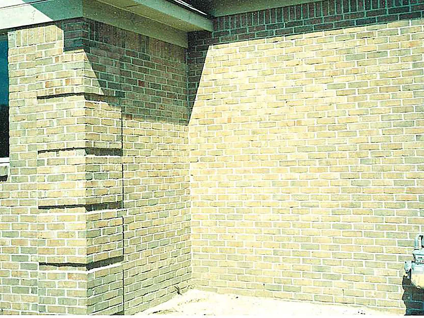The same outside corner in 2003 after staining, the quoin column and the two walls meeting at it reading as one buff and tan blend, the gas meter at the right