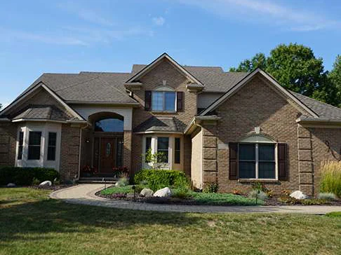 The front of the two-story house in 2019, gabled roofs over a bay window and an arched entry, one buff and tan brick blend across the whole elevation