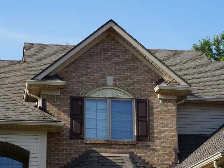 The front gable in 2019 under a clear sky, one even brick blend around the arched window and its dark shutters
