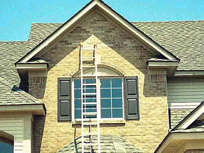 The front gable in 2003 before staining, an extension ladder leaning across its arched window and pale brick showing in the peak