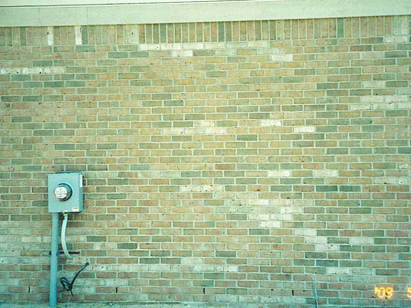 A side wall of the house in May 2003 before staining, pale near-white brick scattered through the buff and tan blend, an electric meter at the left and a window at the right