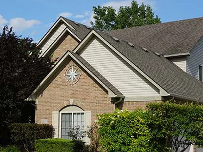 The front of the house in 2019 from the lawn, three stacked gables in tan brick and cream siding, the compass rose on the nearest gable above a shuttered door