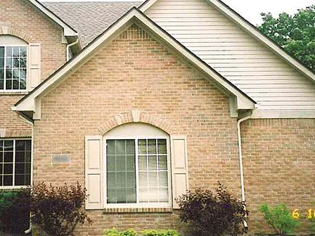 The front gable in 2005 after staining, the brick around the shuttered arched window reading as one tan range, with the camera date 6 10 05 burned into the corner