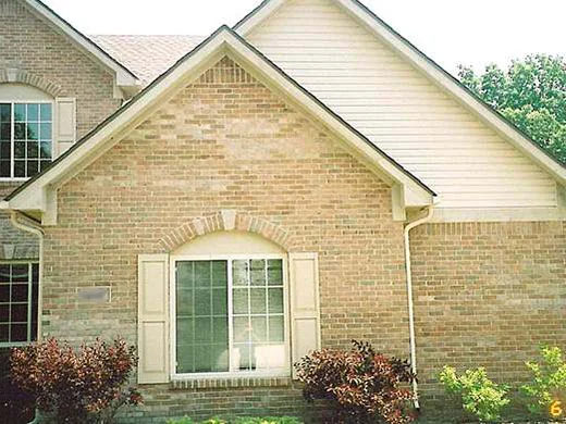 The front gable in 2005 before staining, a shuttered arched window under the gable with light and dark brick scattered unevenly across the face and a van in the drive at the right