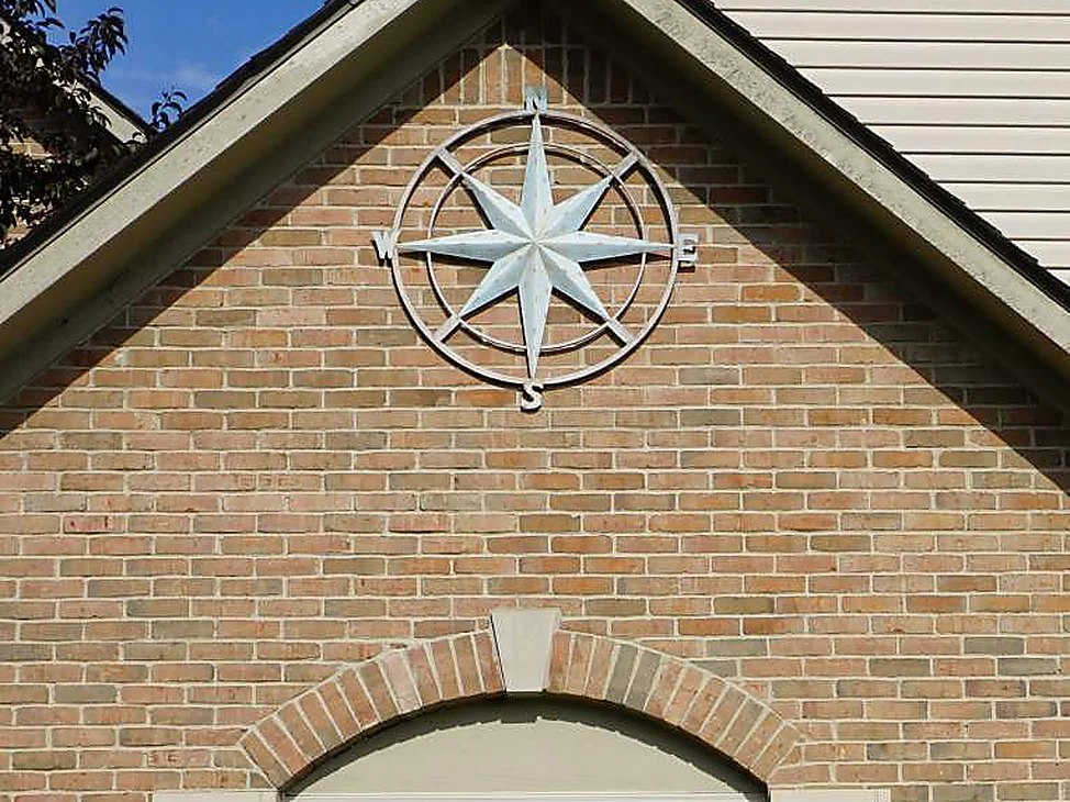 The front gable of the Michigan house in 2019 at close range, a metal compass rose mounted on tan brick above the arched window head