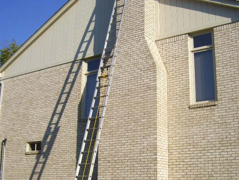 The chimney side of the house in 2011 before staining, white brick with an extension ladder leaning against the wall beside the chimney and cream siding in the gable above