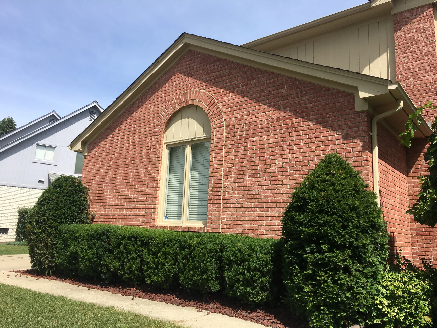 The same gable end in 2019, salmon brick one range from the arched window head to the shrubs, with the cream siding of the upper gable and a grey neighbouring house at the left