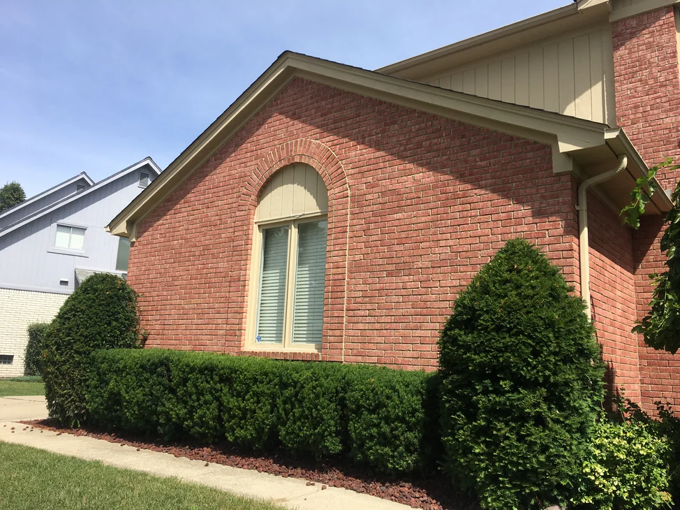 The gable end of the Michigan house in 2019, salmon brick one range from the arched window head to the shrubs under cream siding