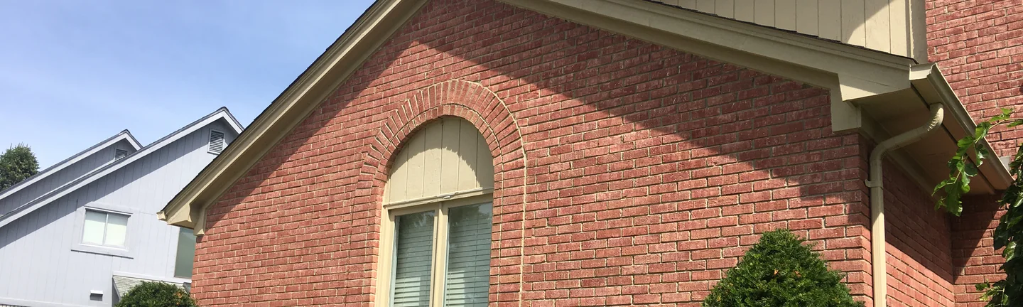 A band of the gable end of the Michigan house in 2019, salmon brick around the head of an arched window