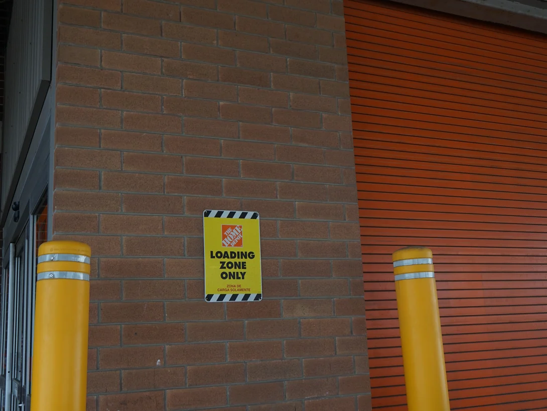 Close view of the brick pier in 2019 beside the orange rolling door, the units running red through tan with a loading zone sign fixed to the face