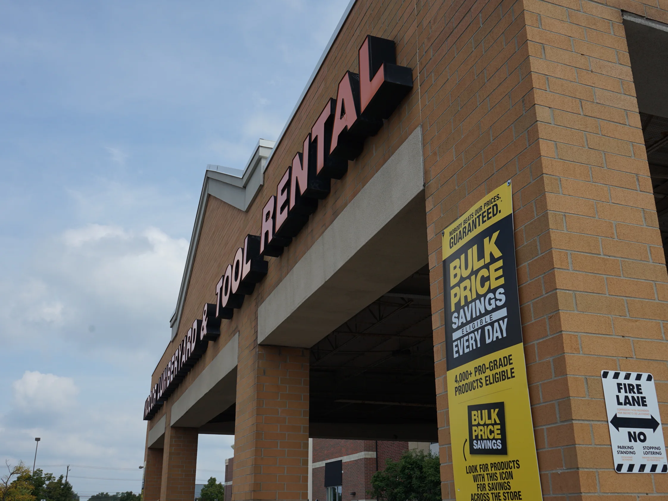 The storefront in 2019 from outside, the sign band running along the parapet and the tan brick piers below it carrying the canopy