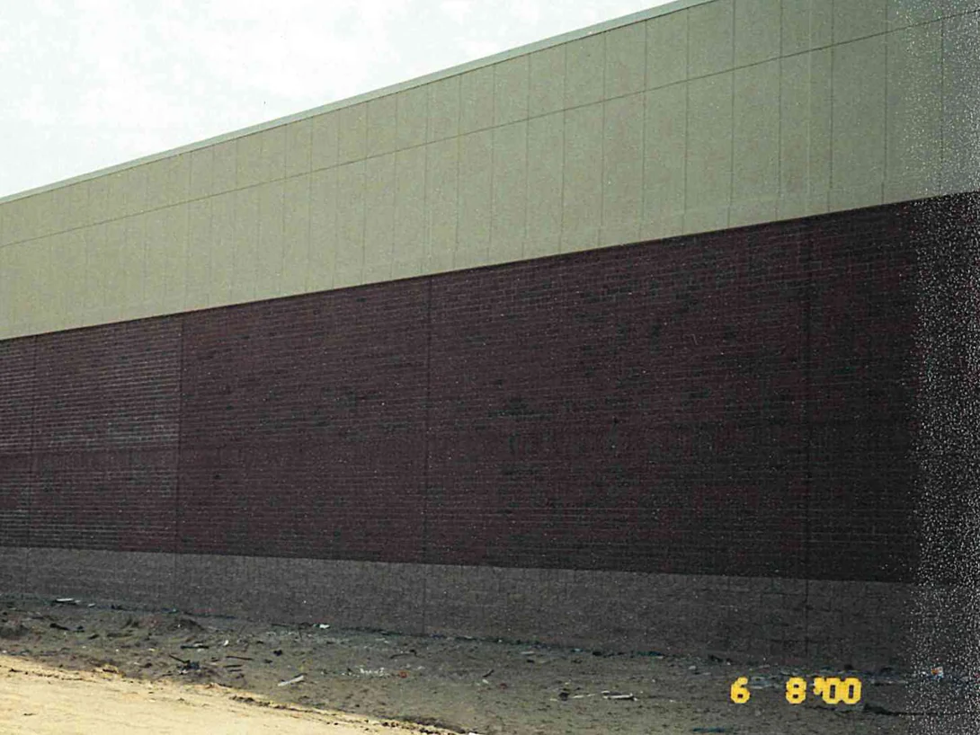 The long side elevation in June 2000, its brick reading dark and flat below a cream precast band, with graded dirt still at the wall and no planting in